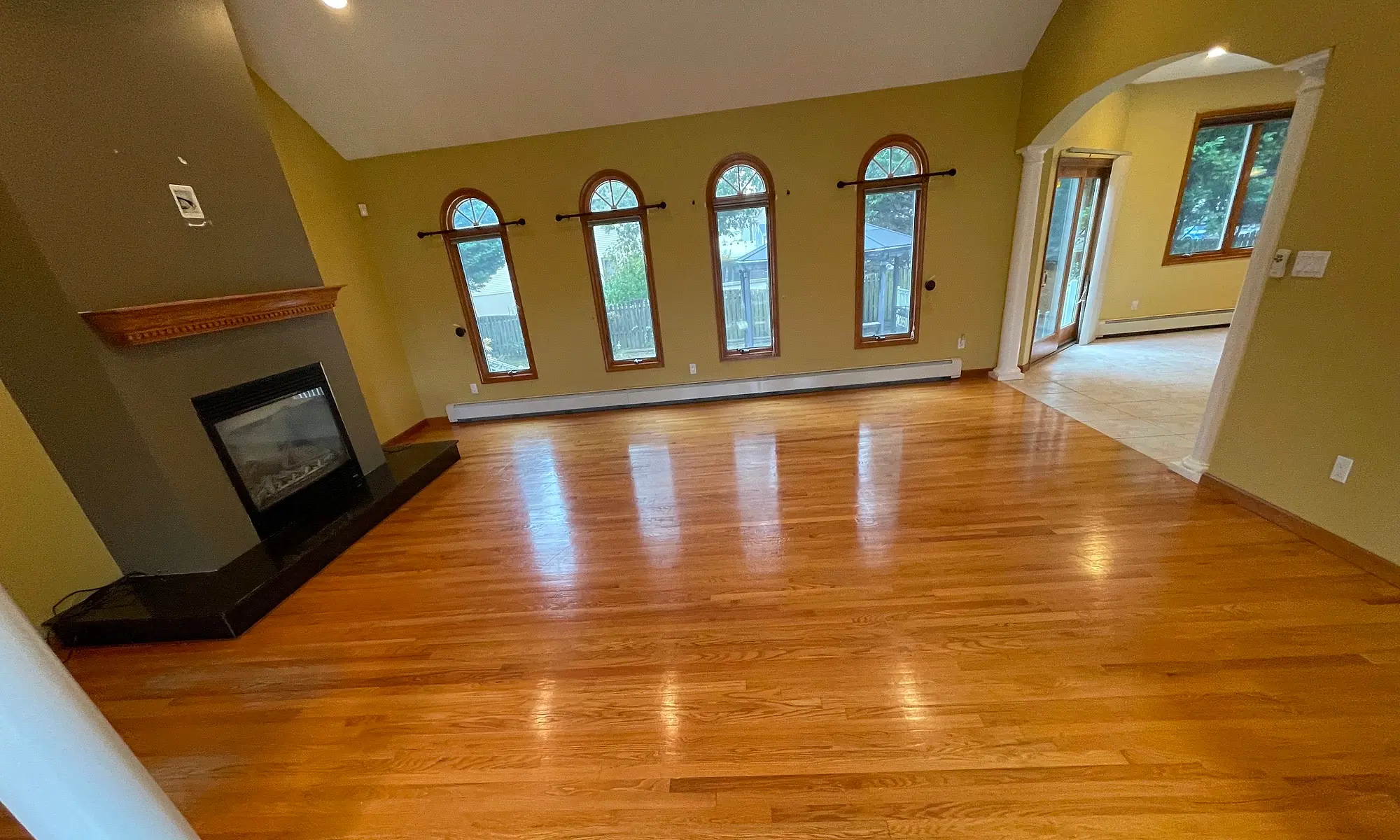 Refinished hardwood floor in a bright living room with a fireplace and arched windows