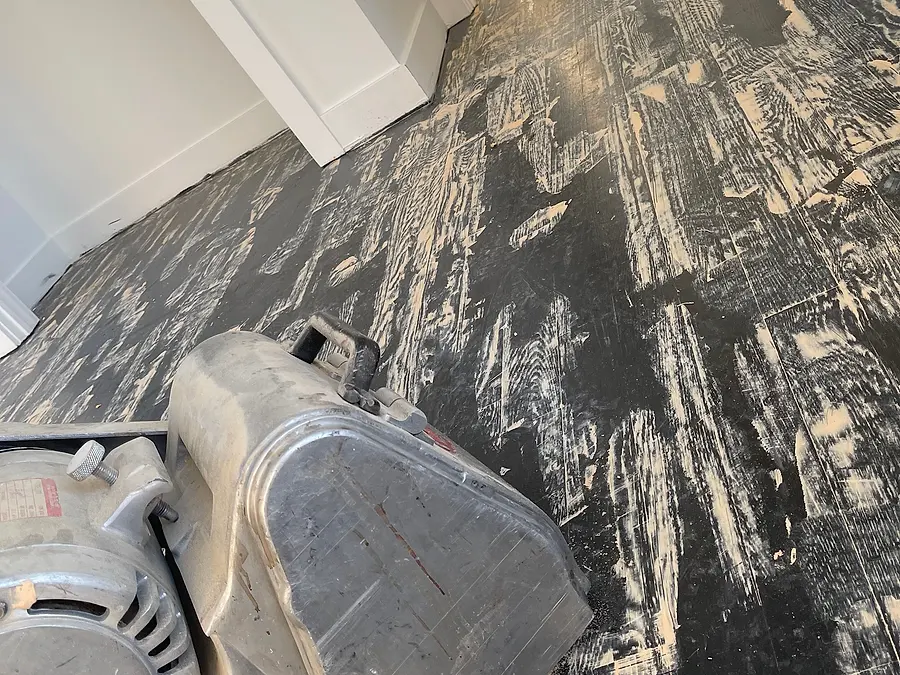 Floor sander removing an old dark coating from a hardwood floor