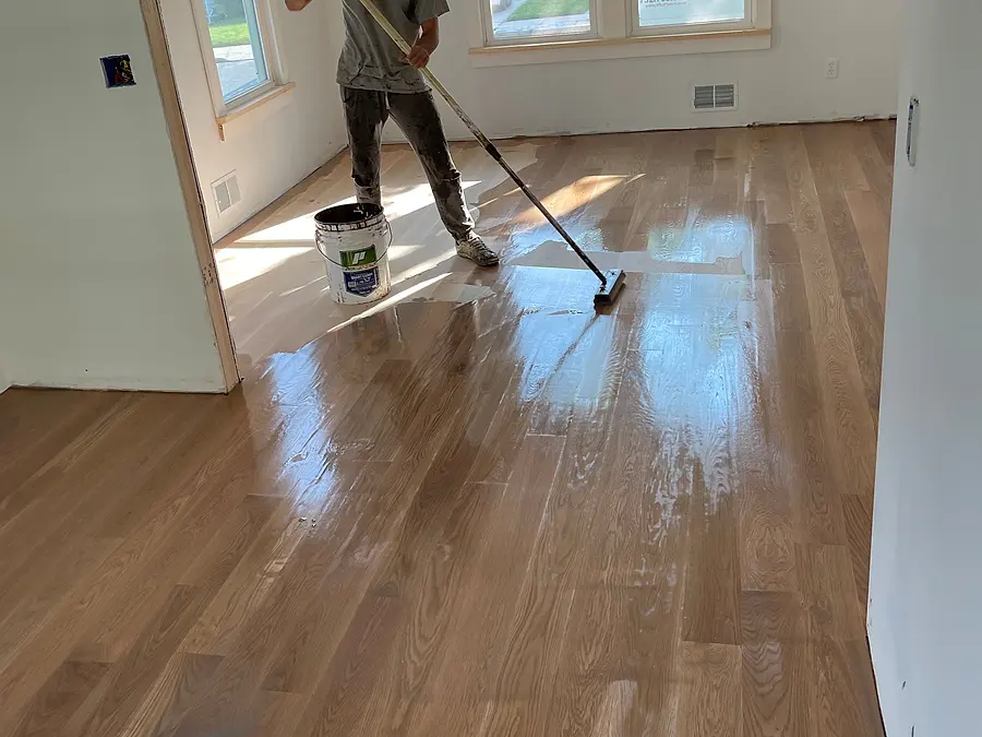 Crew member rolling water-based finish on a hardwood floor
